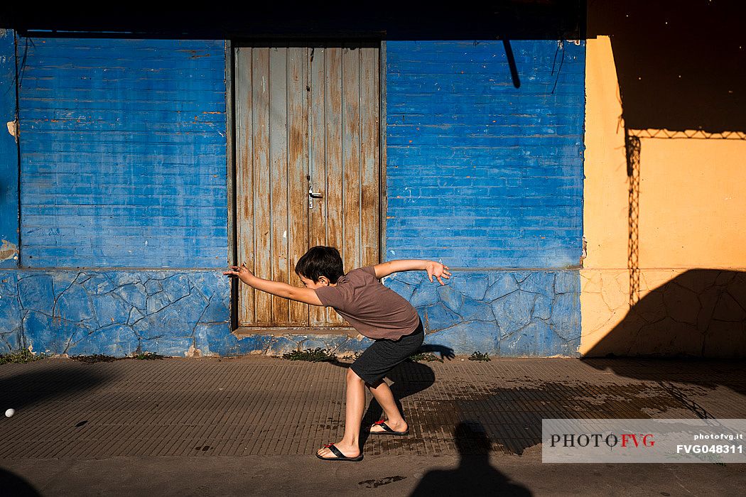 Child plays throwing a ball in the colorful streets of Villa Hayes, Paraguay, America