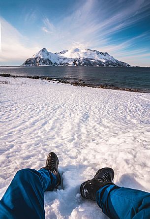 A hiker rests on the beach of Rekvik,a small village near Tromvik, in the background the Sessoya island, Tromso, Norway, Europe
