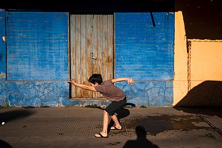 Child plays throwing a ball in the colorful streets of Villa Hayes, Paraguay, America