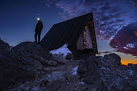 Hikers outside the Luca Vuerich bivouac at twilight, Foronon del Buinz, Montasio mountain range, Julian alps, Friuli Venezia Giulia, Italy, Europe