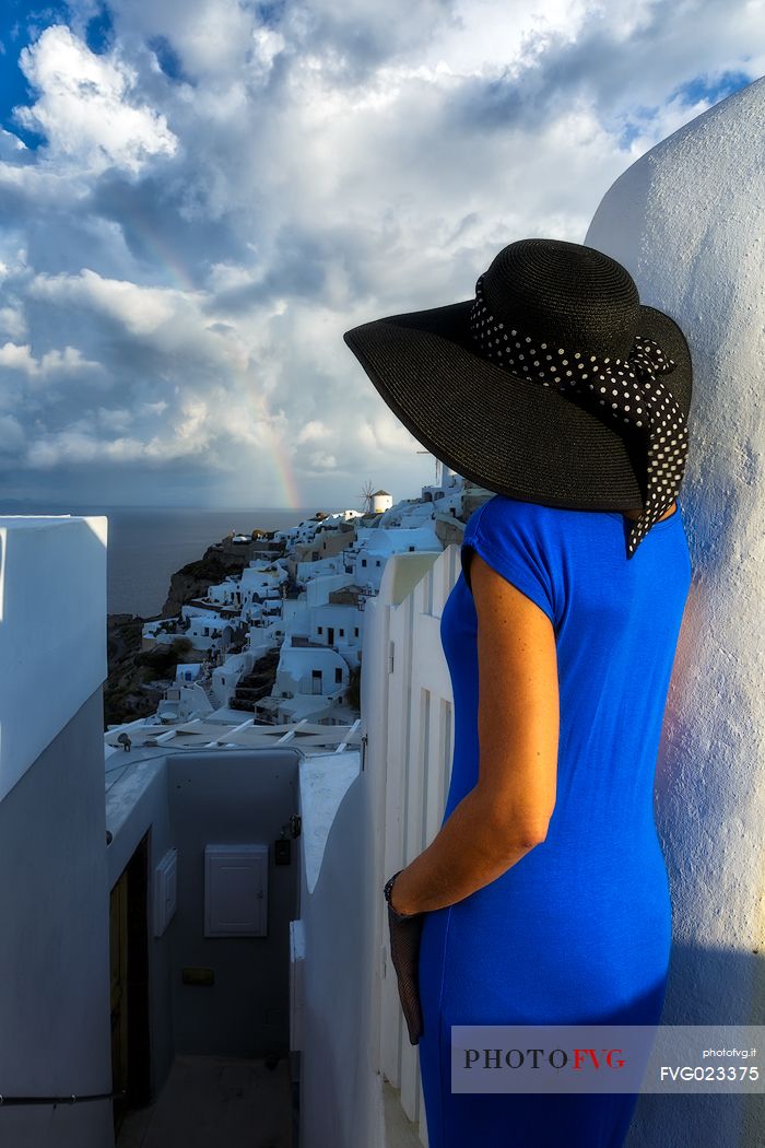Panoramic view of Santorini island from old church ruins in Oia with a model in blue dress color.Rainbow time,Greece