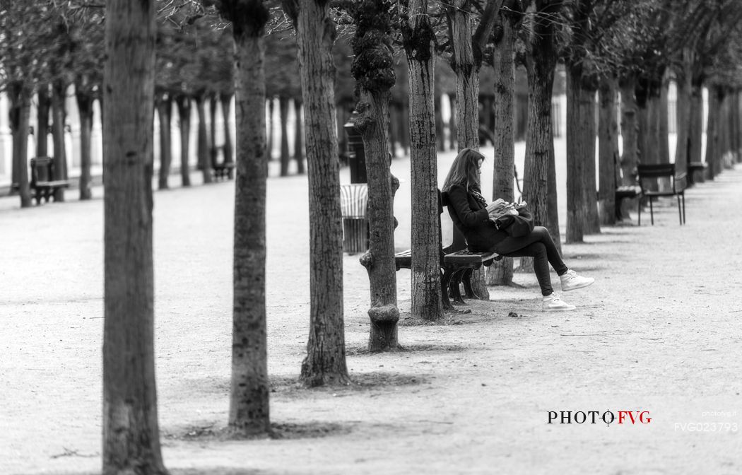 One girl seated is reading a book.Palais Royale. Paris, France