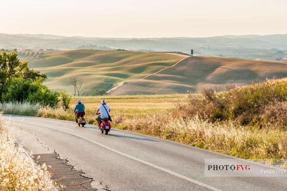On the road with Vespa in the Crete Senesi landscape, Orcia valley, Tuscany, Italy