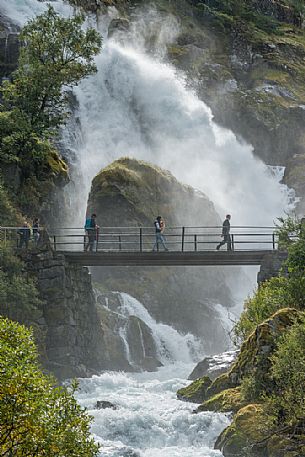 Tourist on the bridge of Briksdalsbreen waterfalls, popular touristic hike to Briksdal glacier, Norway